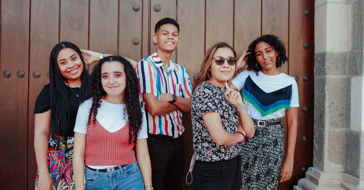 Five diverse young adults smiling while posing by a large wooden door, exuding joy and friendship.